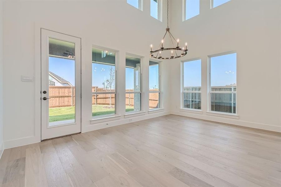 Unfurnished dining area with a notable chandelier, a towering ceiling, and light hardwood / wood-style flooring