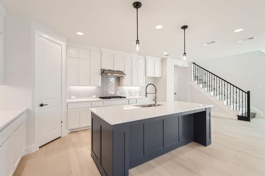 Kitchen with a kitchen island with sink, sink, decorative light fixtures, light wood-type flooring, and white cabinets