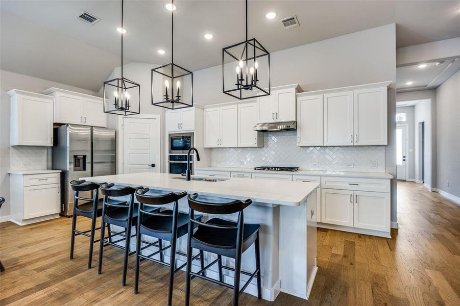 Kitchen featuring an island, lantern pendant lighting, stainless steel appliances, and white cabinetry