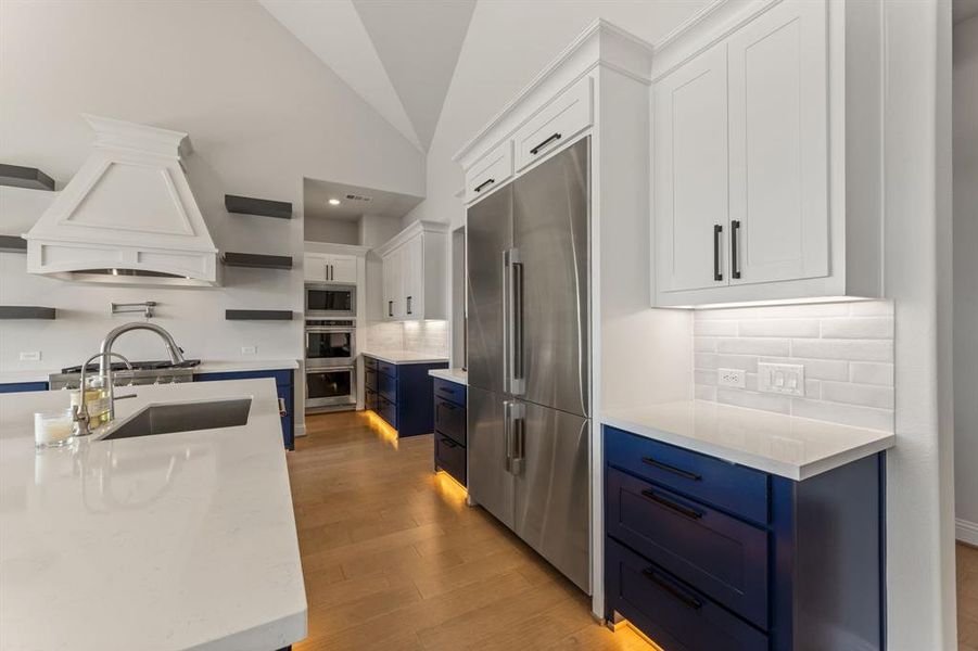 Kitchen with white cabinetry, vaulted ceiling, built in appliances, blue cabinetry, and sink