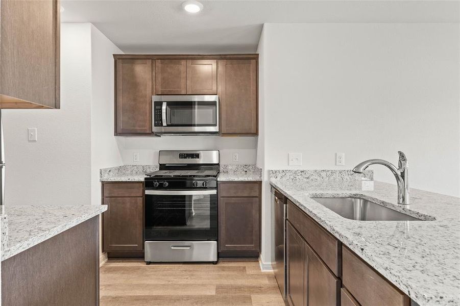 Kitchen with light hardwood / wood-style floors, stainless steel appliances, sink, and light stone counters