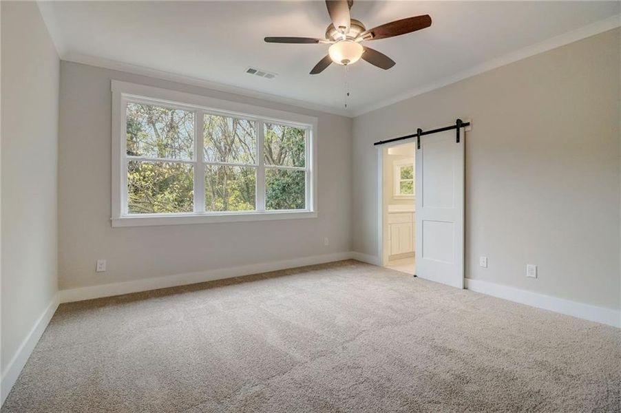 Empty room featuring ornamental molding, light carpet, ceiling fan, and a barn door