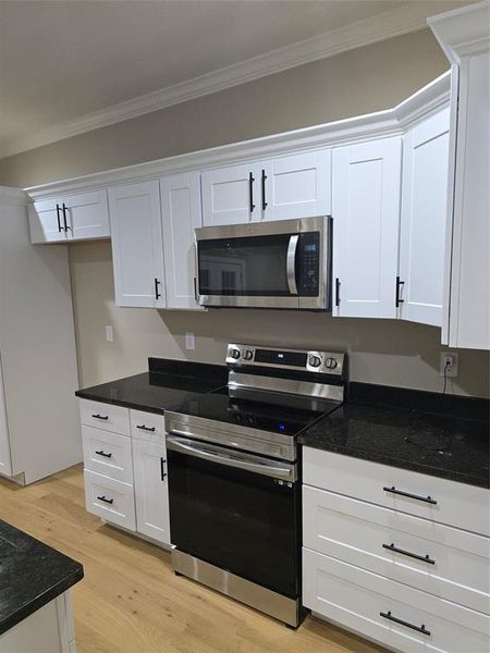 Kitchen with stainless steel appliances, crown molding, light hardwood / wood-style floors, and white cabinetry