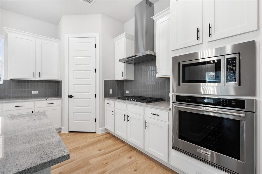 Kitchen includes built-in microwave and oven, along with black iron cooktop and stainless-steel vent hood.