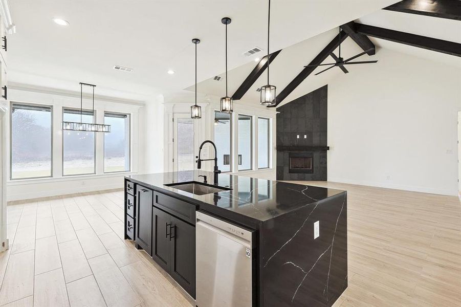 Kitchen featuring sink, stainless steel dishwasher, light hardwood / wood-style flooring, a center island with sink, and lofted ceiling with beams