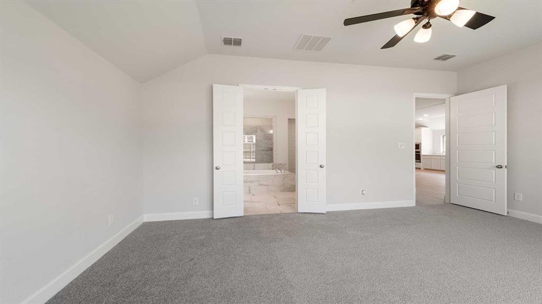 Unfurnished bedroom with carpet floors, ensuite bath, ceiling fan, and vaulted ceiling