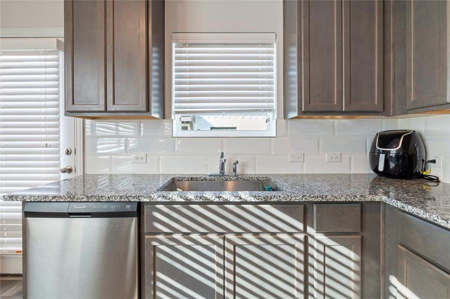 Kitchen with sink, tasteful backsplash, dark brown cabinets, dishwasher, and light stone countertops