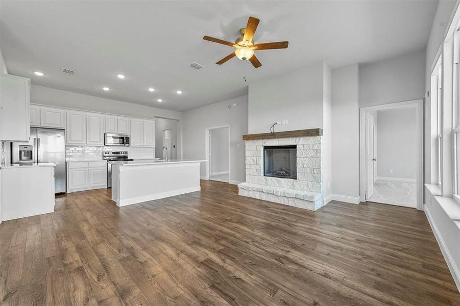 Unfurnished living room with a stone fireplace, ceiling fan, sink, and dark wood-type flooring
