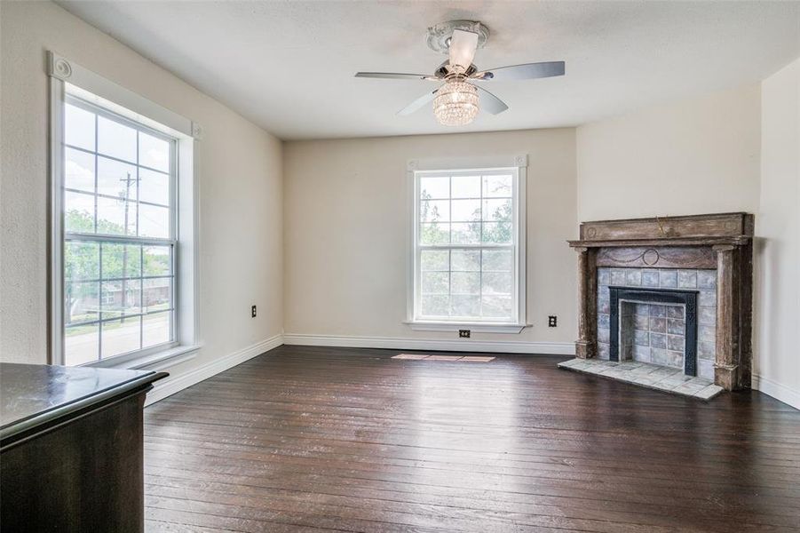 Unfurnished living room featuring a tile fireplace, a healthy amount of sunlight, dark hardwood / wood-style flooring, and ceiling fan