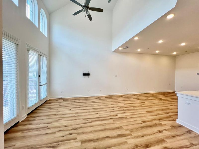 Unfurnished living room featuring plenty of natural light, light hardwood / wood-style floors, ceiling fan, and a high ceiling