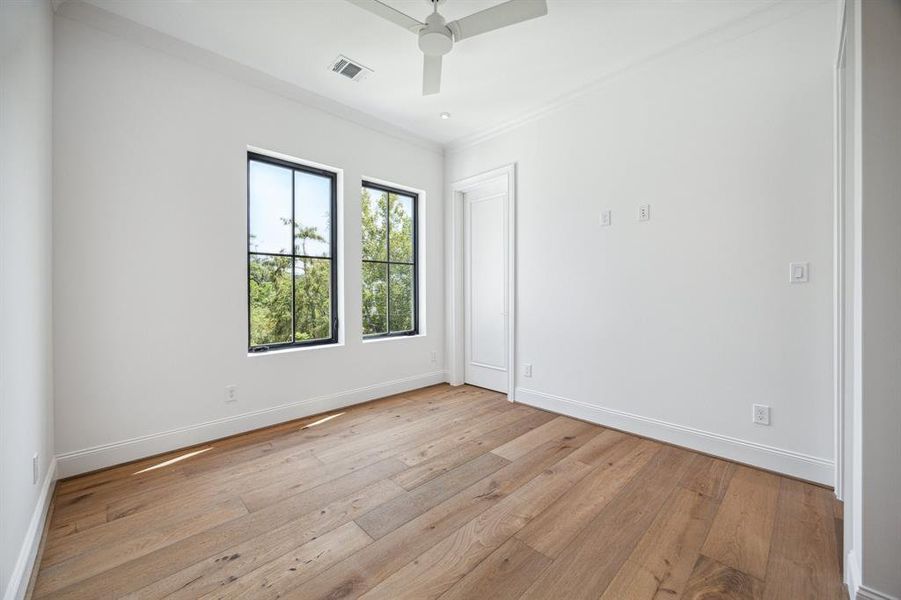 The third of four secondary bedrooms features European white oak flooring, a spacious walk-in closet, and a private ensuite bathroom. With a designer ceiling fan and tree top views, the room is filled with natural light, offering both comfort and style.