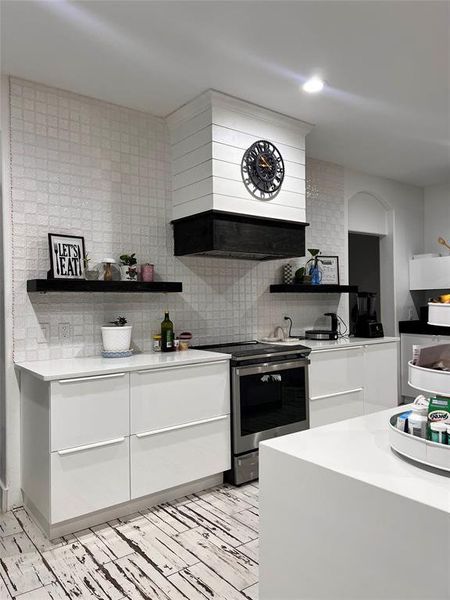 Kitchen featuring backsplash, electric range, custom exhaust hood, white cabinets, and light tile patterned flooring