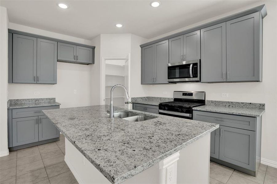 Kitchen featuring a center island with sink, appliances with stainless steel finishes, and light tile flooring