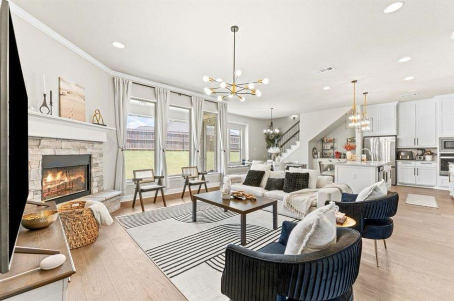 Living room with ornamental molding, sink, a stone fireplace, a chandelier, and light wood-type flooring