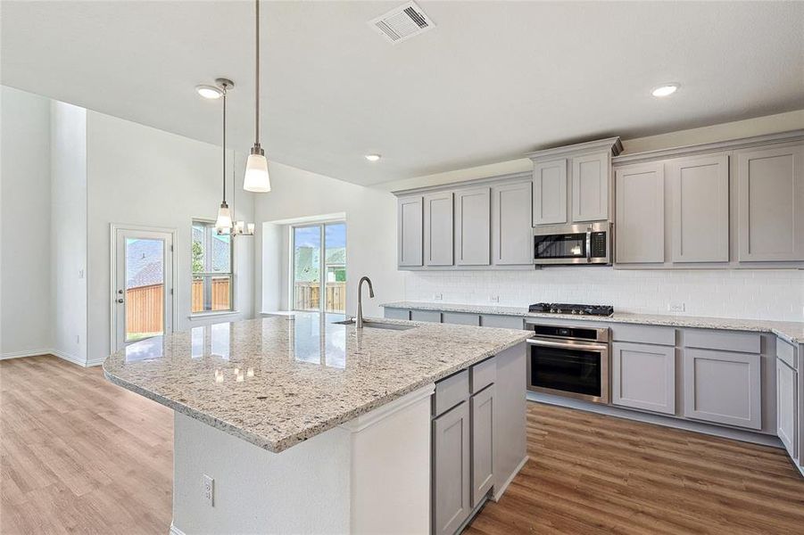 Kitchen featuring stainless steel appliances, sink, light wood-type flooring, and an island with sink