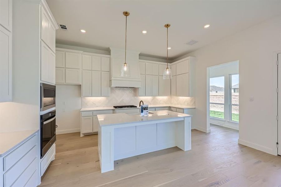 Kitchen with white cabinets, a center island with sink, backsplash, light hardwood / wood-style flooring, and stainless steel appliances