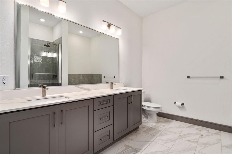 Bathroom with tile patterned flooring, double sink vanity, toilet, and a shower with door