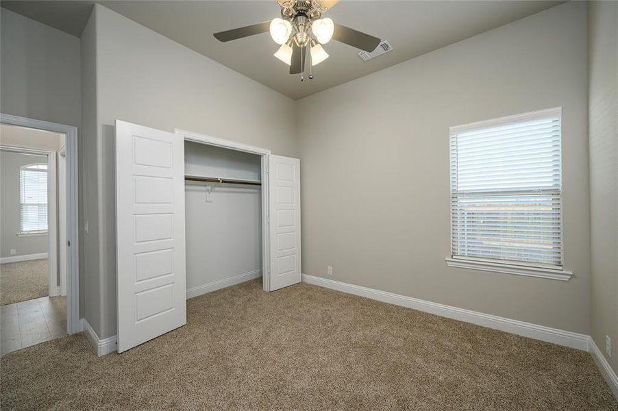 Unfurnished bedroom with a closet, light carpet, multiple windows, and ceiling fan