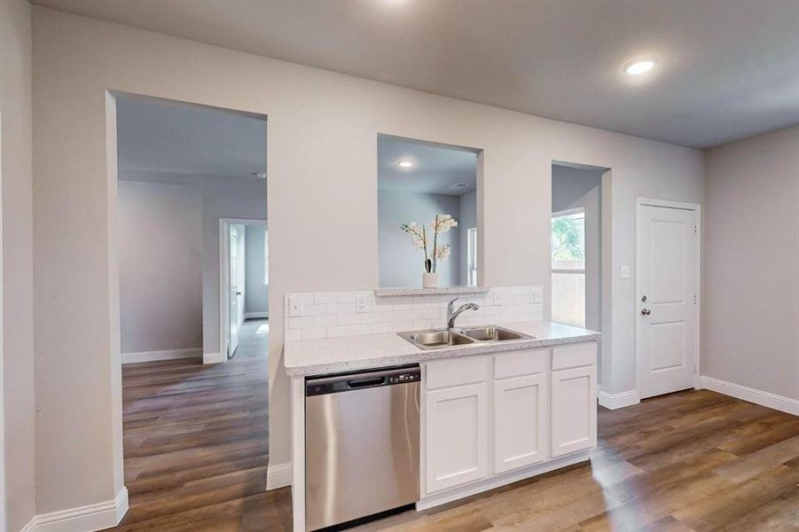 Kitchen with white cabinets, backsplash, wood-type flooring, dishwasher, and sink