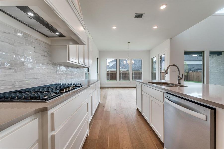 Kitchen with sink, stainless steel appliances, pendant lighting, white cabinets, and light hardwood / wood-style flooring