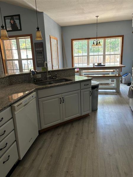 Kitchen with white cabinets, hanging light fixtures, dishwashing machine, hardwood / wood-style floors, and sink