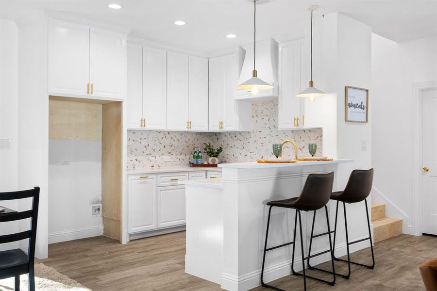 Kitchen featuring pendant lighting, light hardwood / wood-style flooring, backsplash, custom range hood, and white cabinets