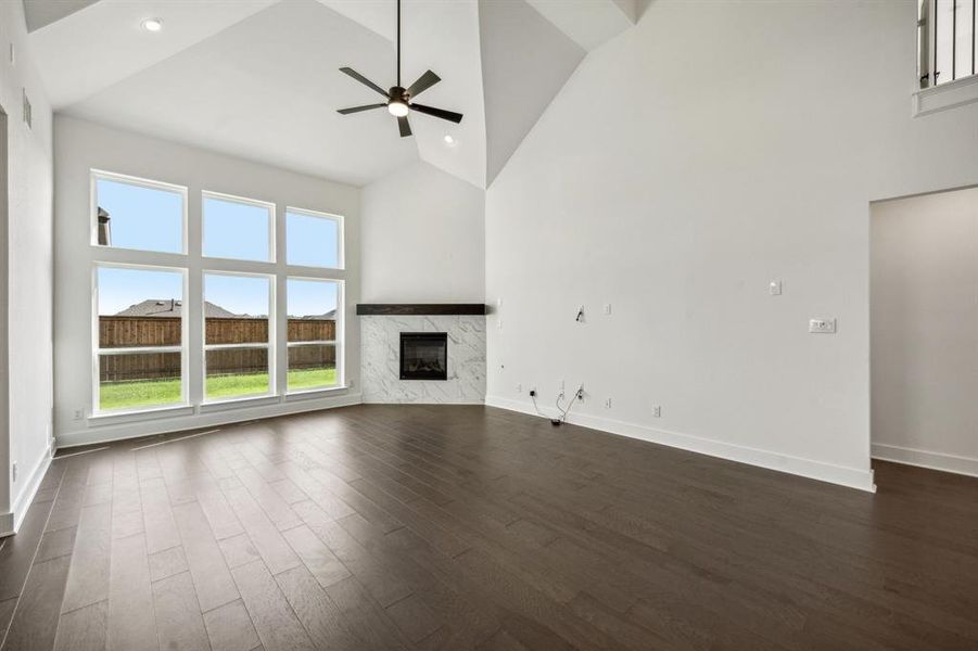 Unfurnished living room with a premium fireplace, high vaulted ceiling, ceiling fan, and dark hardwood / wood-style floors