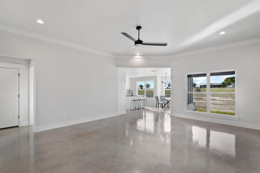 Living room featuring crown molding, ceiling fan with notable chandelier, and concrete flooring