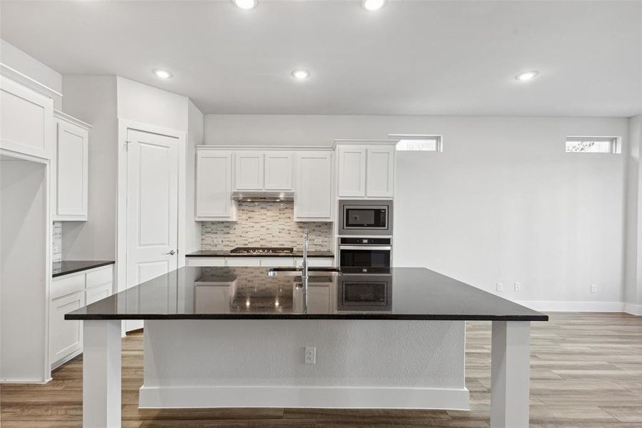 Kitchen featuring appliances with stainless steel finishes, white cabinetry, a kitchen island with sink, and tasteful backsplash