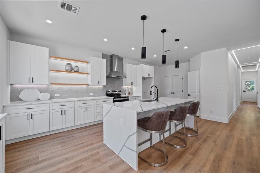 Kitchen with white cabinets, a center island with sink, and wall chimney range hood