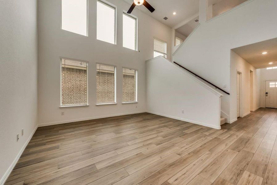 Unfurnished living room featuring ceiling fan, a high ceiling, and light hardwood / wood-style floors