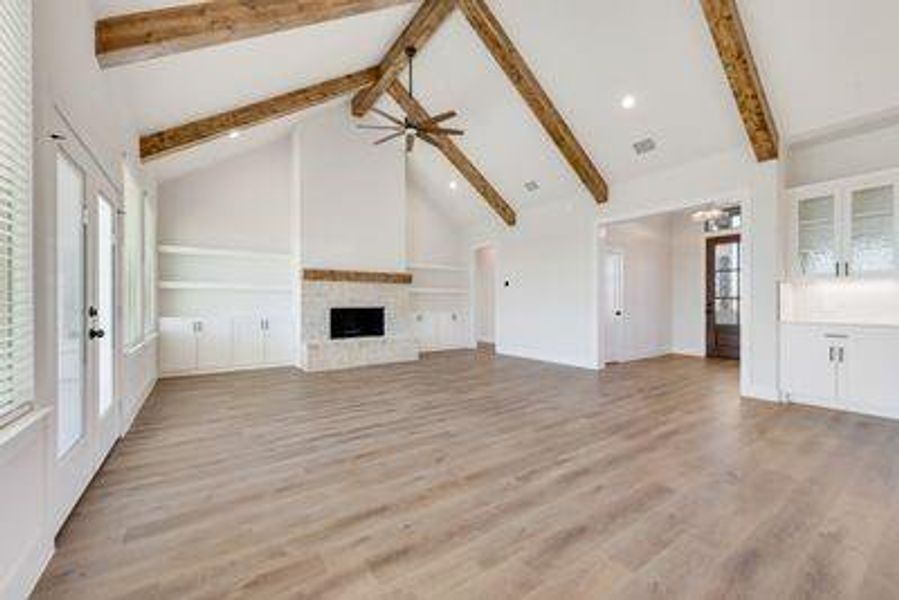 Unfurnished living room featuring light hardwood / wood-style floors, beam ceiling, a fireplace, and a wealth of natural light