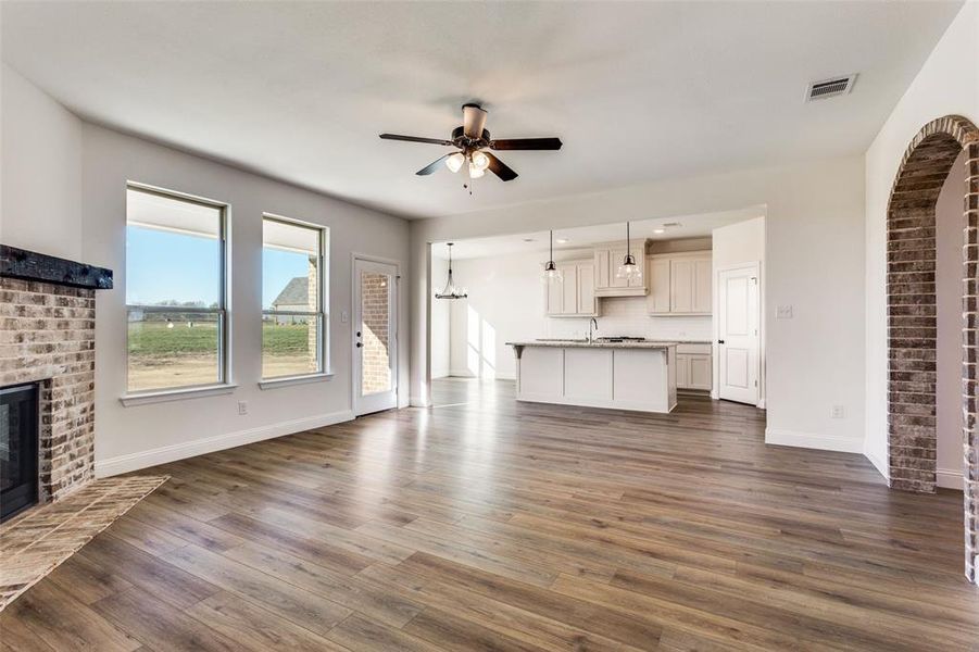 Unfurnished living room with a brick fireplace, ceiling fan, and dark wood-type flooring