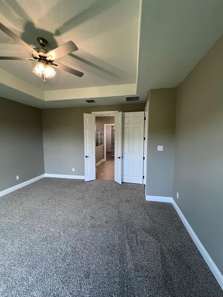 Unfurnished bedroom with ceiling fan, a raised ceiling, and dark carpet
