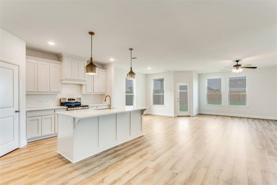 Kitchen with decorative backsplash, sink, a center island with sink, stainless steel range, and light hardwood / wood-style flooring