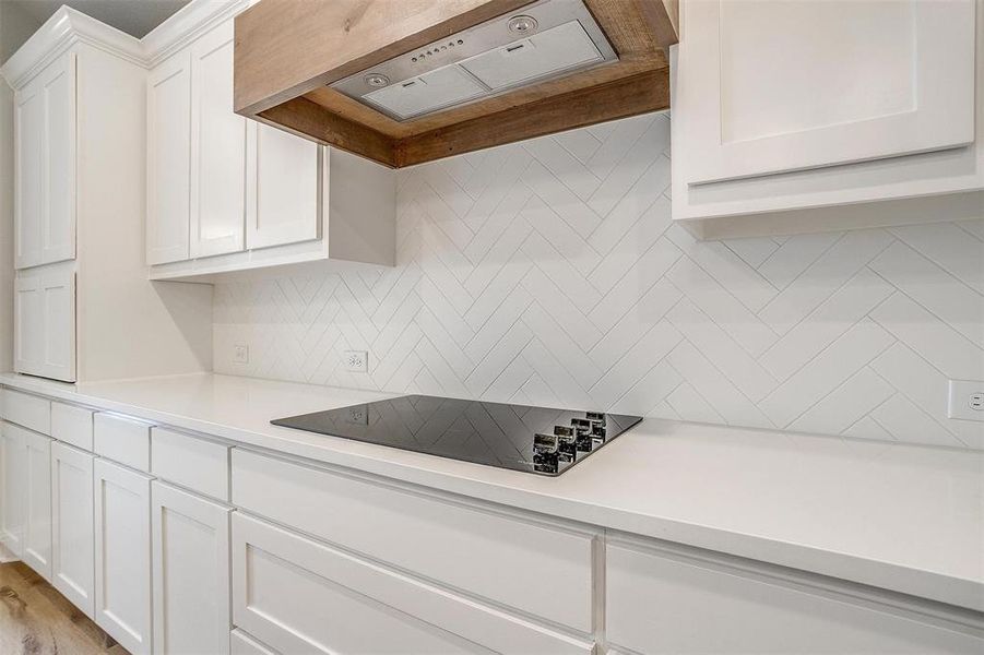 Kitchen featuring white cabinets, light hardwood / wood-style floors, decorative backsplash, black electric cooktop, and custom range hood