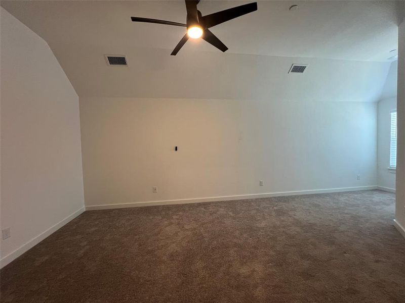 Carpeted empty room featuring ceiling fan and vaulted ceiling