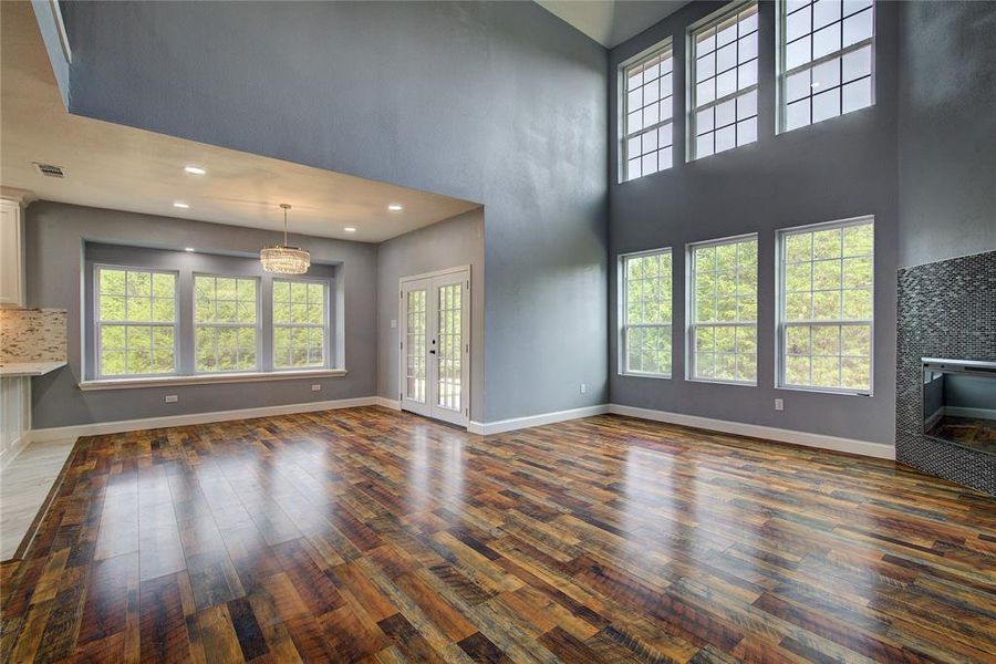 Unfurnished living and dining with dark hardwood / wood-style floors, a healthy amount of sunlight, and a towering ceiling