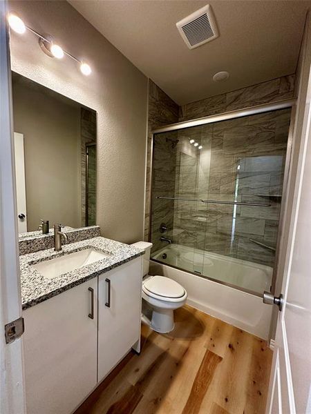 Full bathroom featuring vanity, wood-type flooring, shower / bath combination with glass door, and toilet