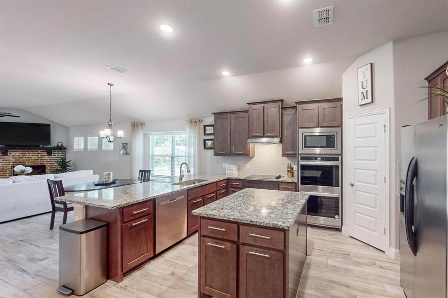 Kitchen with stainless steel appliances, light stone countertops, and light wood-type flooring