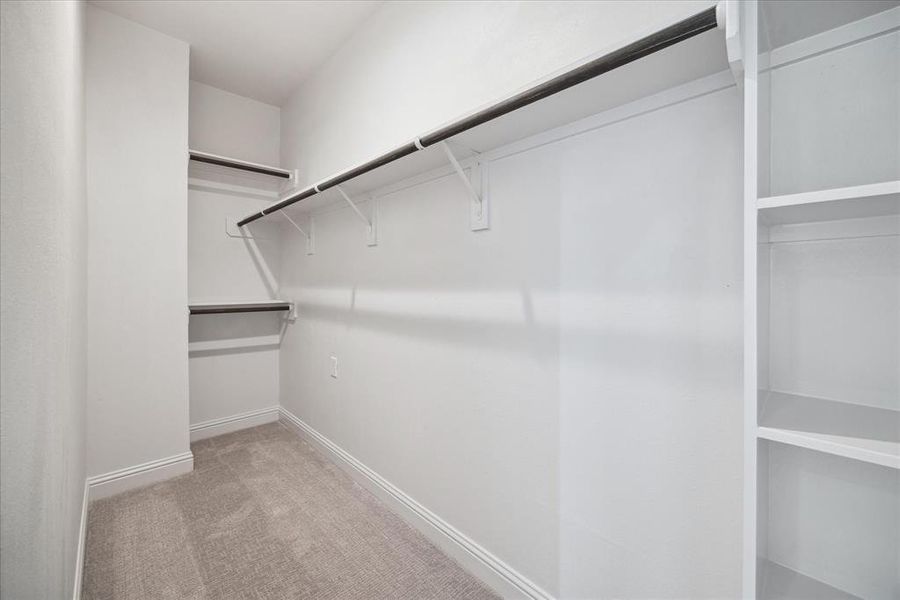 This spacious primary walk-in closet, located ensuite, offers ample storage with built-in shelving and double hanging rods.