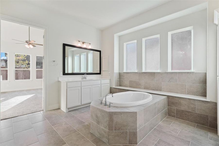 Bathroom with vanity, tile patterned flooring, ceiling fan, and tiled bath