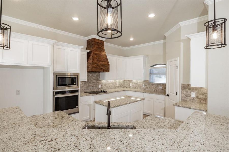 Kitchen with white cabinetry, stainless steel appliances, hanging light fixtures, and sink