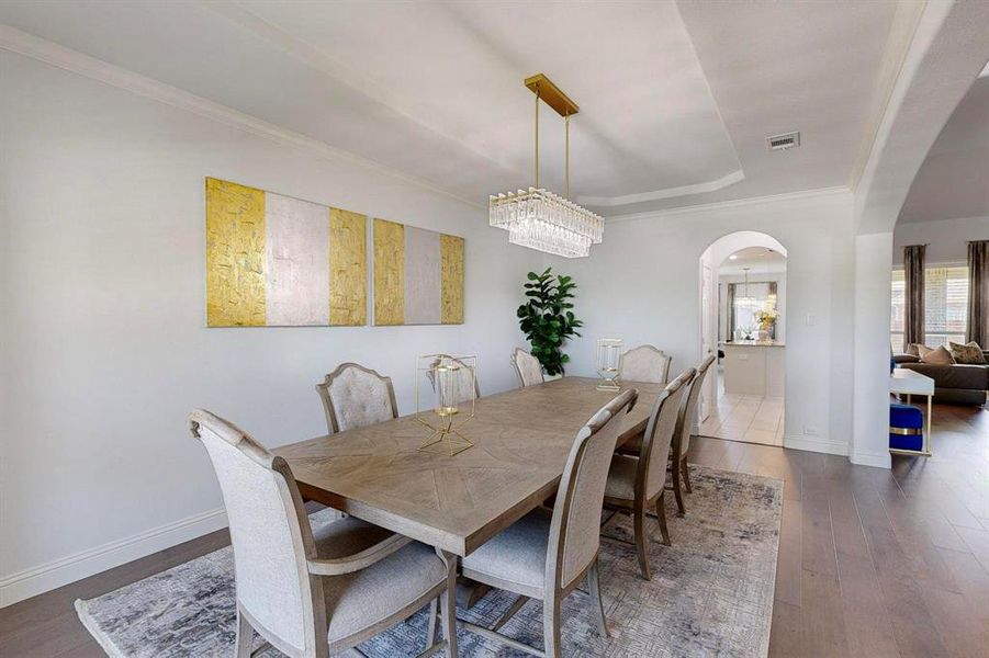 Dining space with dark wood-type flooring, crown molding, and a chandelier