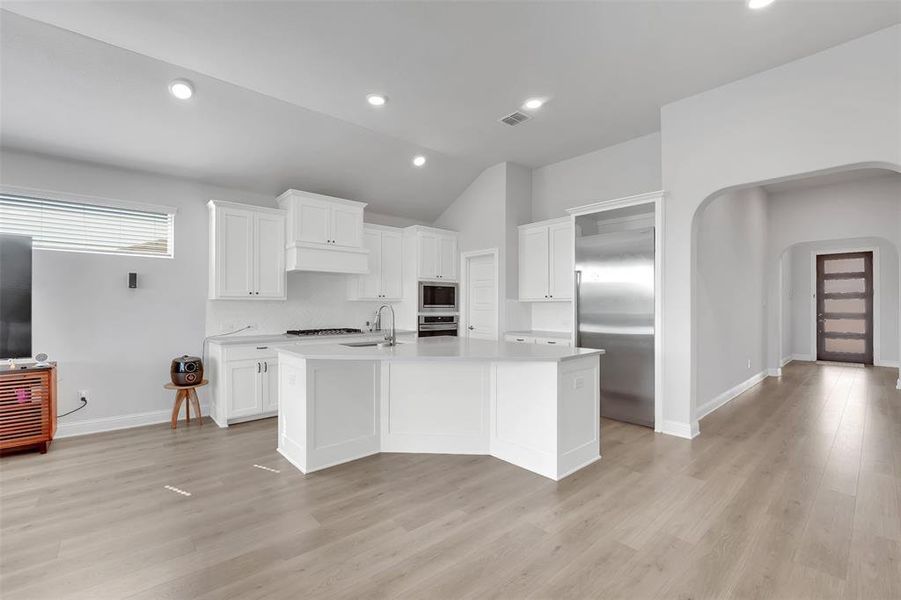 Kitchen with a kitchen island with sink, lofted ceiling, built in appliances, and white cabinetry