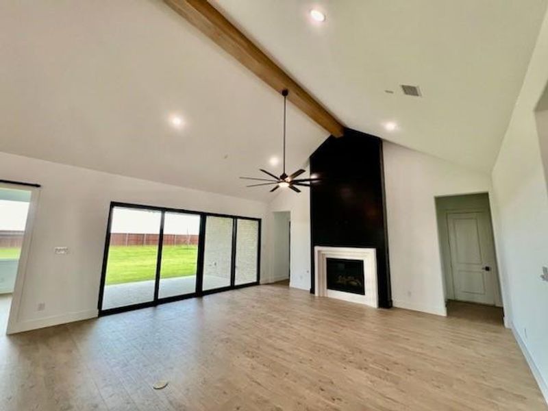 Unfurnished living room featuring high vaulted ceiling, light hardwood / wood-style flooring, a wealth of natural light, and beam ceiling