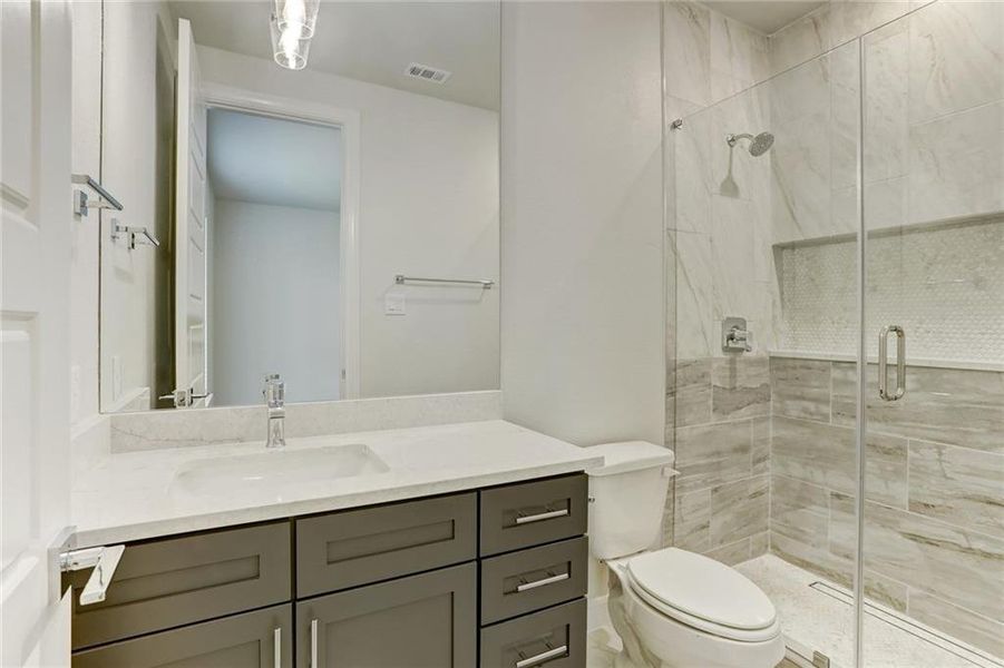 The in-law suite bathroom has a spacious walk-in shower and quartz vanity with a full mirror that spans to the ceiling.