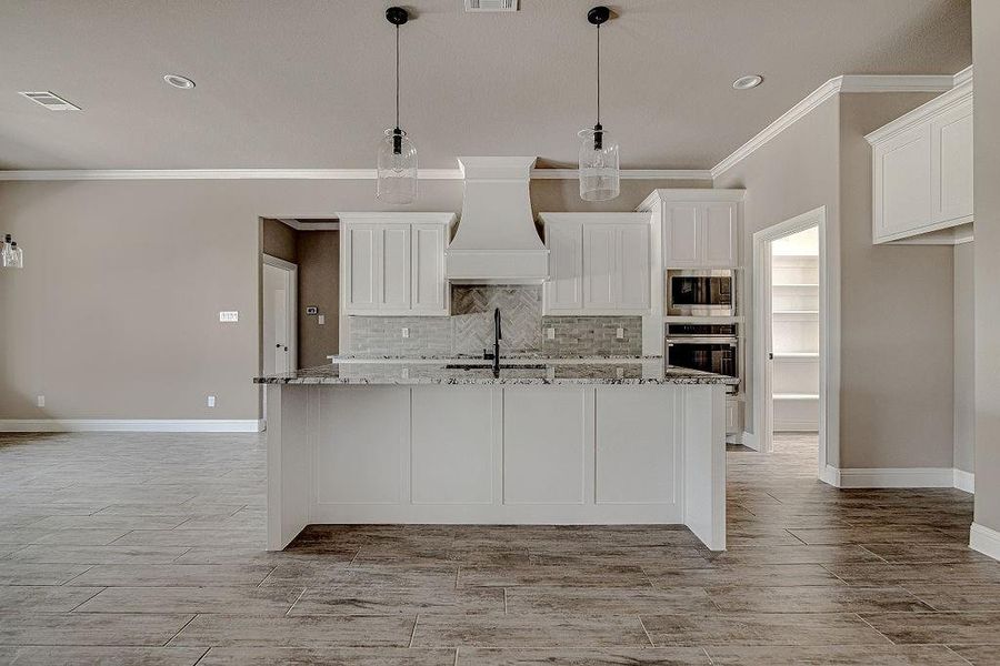 Kitchen featuring stainless steel appliances, light stone countertops, custom range hood, and a center island with sink