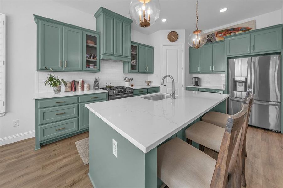 Kitchen featuring sink, appliances with stainless steel finishes, decorative light fixtures, a kitchen island with sink, and light hardwood / wood-style flooring