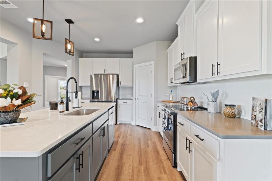 Kitchen featuring white cabinetry, an island with sink, pendant lighting, stainless steel appliances, and light wood-type flooring